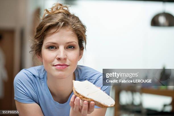 portrait of a woman eating toast with cream spread on it - woman eating toast stock pictures, royalty-free photos & images