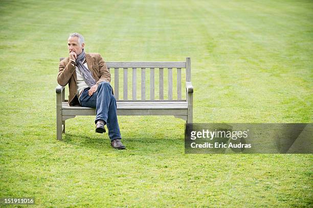 man sitting on a bench and thinking in a park - mann lässig gras sitzen stock-fotos und bilder