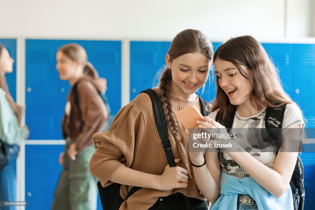Teenage girls using smart phone in school corridor
