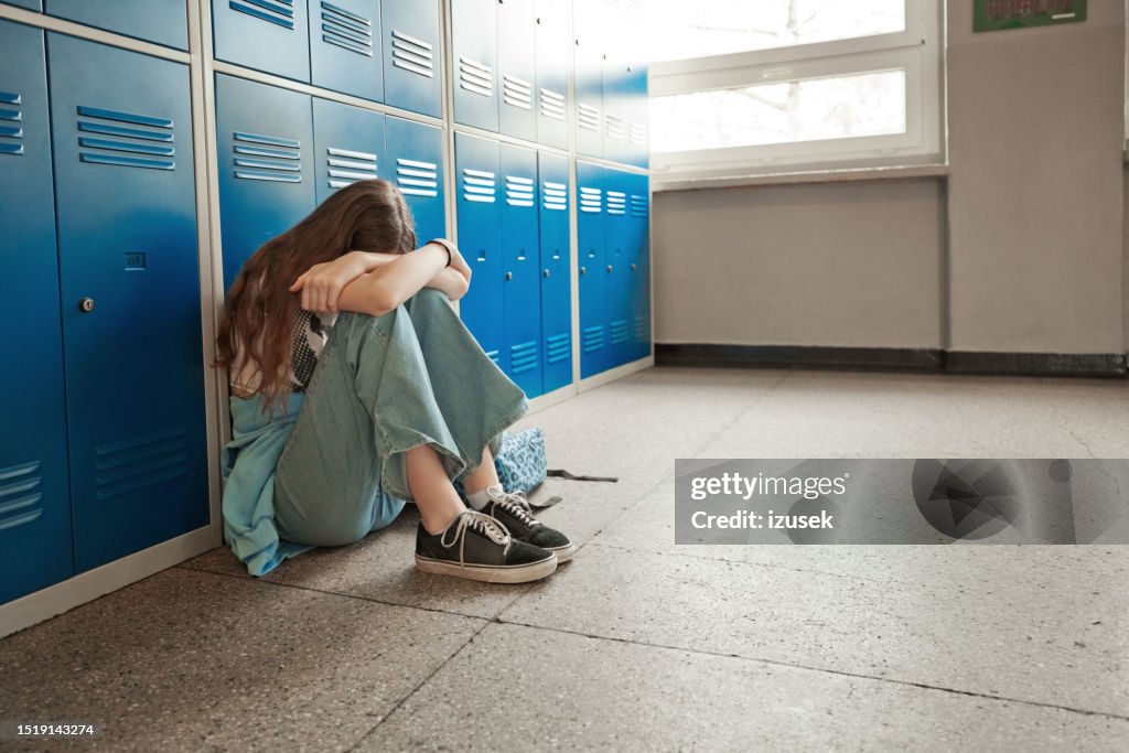 Adolescente preocupada sentada en el suelo de la escuela