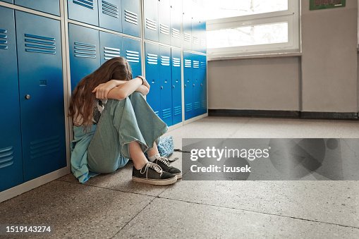 Worried teenage girl sitting on floor at school Worried teenage girl sitting on floor at school