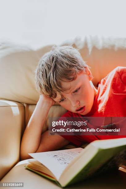 a little boy lies on his side on a sofa, and reads a book - annual event stock pictures, royalty-free photos & images