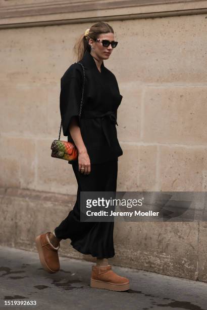 Veronika Heilbrunner seen wearing black sunglasses, black kimono shaped jacket, black silk long skirt, gold choker necklace and earrings, colorful...