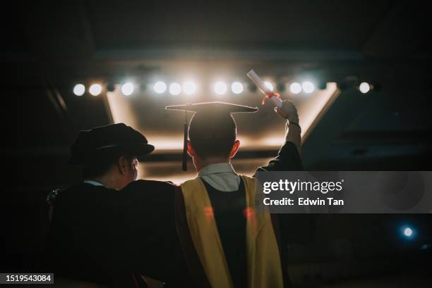 convocation ceremony excited asian graduation university student arm raised standing beside dean after received graduation scroll on auditorium stage - graduation podium stockfoto's en -beelden