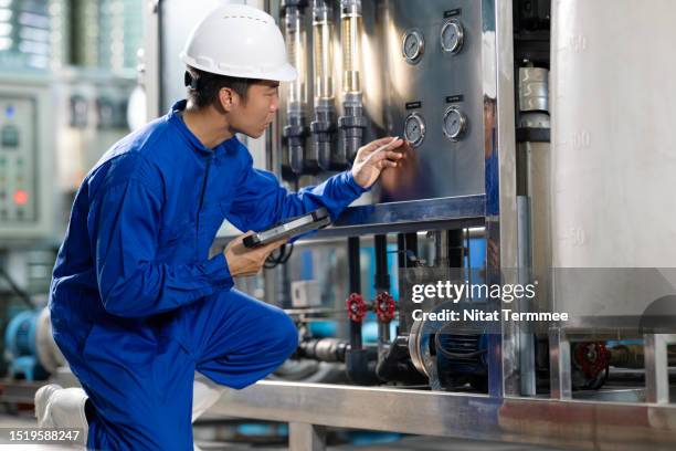 ingredient and filtration water solutions for a bottling industry to ensure quality of mineral water products. side view of a japanese stationary engineer examining a pressure gauge on ingredient water storage and distribution process for water bottling. - water margin stock pictures, royalty-free photos & images