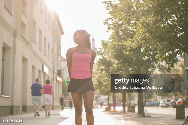 captivating young black lady in pink top and short black skirt strolling along quiet city street - beautiful perfection exposed lady stock pictures, royalty-free photos & images