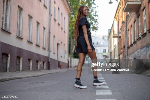 lovely young black woman in stylish black dress and sneakers finds joy in quiet ambiance of deserted street - ambiance girly stock pictures, royalty-free photos & images