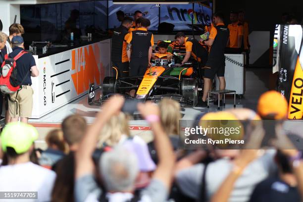 Fans look on as Lando Norris of Great Britain and McLaren has a seat fitting in the garage during previews ahead of the F1 Grand Prix of Great...