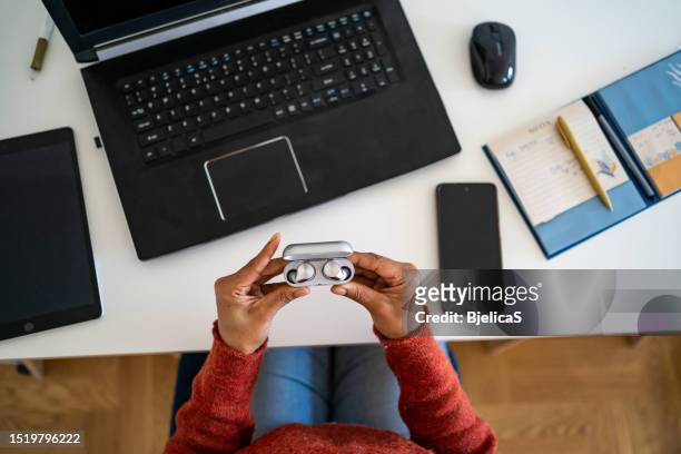 woman using wireless in-ear headphones while working from home - bluetooth headphones stock pictures, royalty-free photos & images