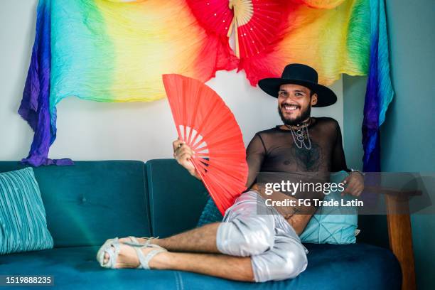 portrait of young gay man with hand fan in the living room at home - cross dressing stock pictures, royalty-free photos & images