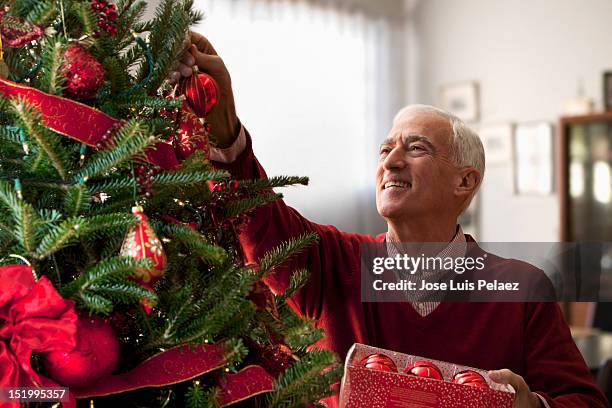 senior man decorating christmas tree - kerstboom versieren stockfoto's en -beelden