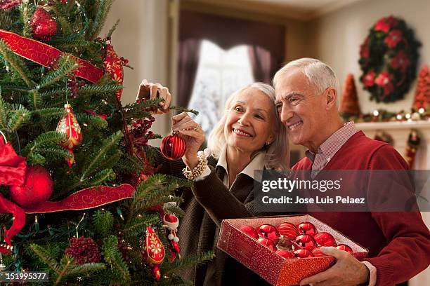 senior couple decorating christmas tree - kerstboom versieren stockfoto's en -beelden