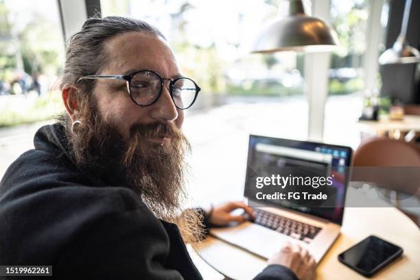 portrait of a mid adult man working using laptop at coffee shop - emo guy stock pictures, royalty-free photos & images