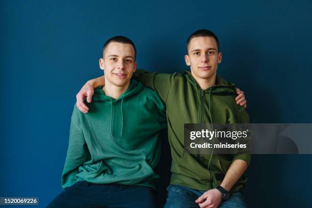 retrato de irmãos gêmeos felizes abraçando na frente de um fundo azul - gêmeos nascimento múltiplo - fotografias e filmes do acervo