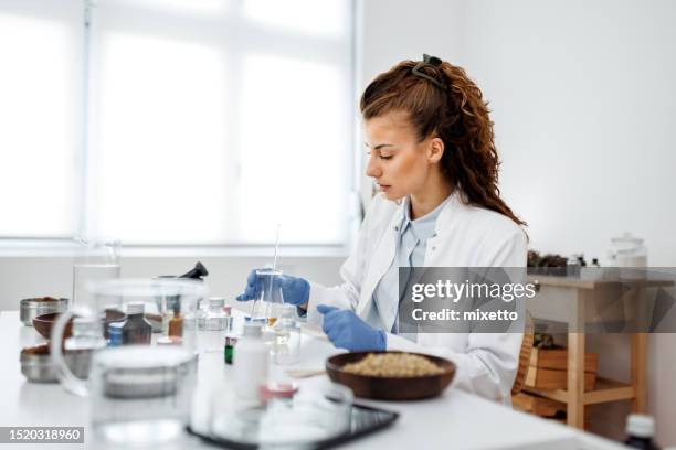 young beautiful woman wearing lab coat making organic cosmetic products at her home workshop - natural organics stock pictures, royalty-free photos & images