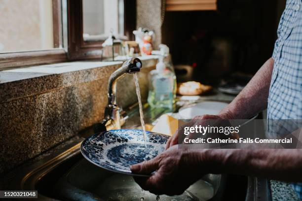 a man rinses a plate underneath a tap in a kitchen - scourer stock pictures, royalty-free photos & images