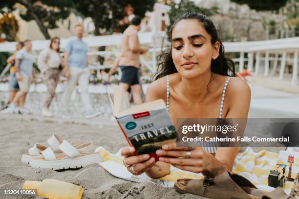 a woman lies on her stomach and reads a travel book on a beach - jet lag stockfoto's en -beelden