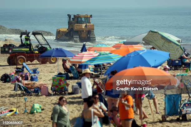 People crowd the beach as contractors with the Army Corp of Engineers move sand as it is pumped from the ocean as part of a beach and dune...