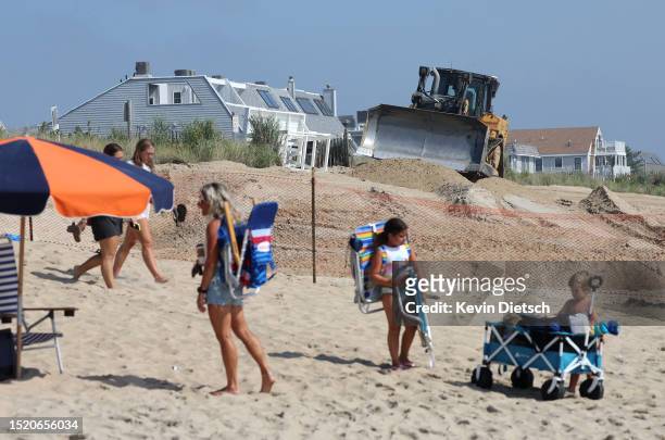 People walk on the beach as contractors with the Army Corp of Engineers move sand as it is pumped from the ocean as part of a beach and dune...