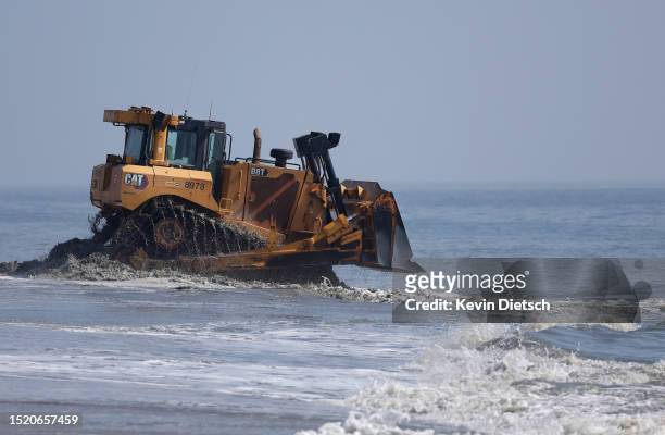 Contractors with the Army Corp of Engineers move sand as it is pumped from the ocean as part of a beach and dune replenishment project on July 06,...