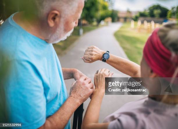 mature couple in sports wear jogging together and checking the time at smartwatch - pedometer stock pictures, royalty-free photos & images