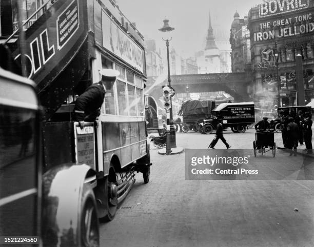 Conductor leans out from the rear platform of a bus waiting at trarfic lights on Ludgate Circus, where Farringdon Street and New Bridge Street cross...