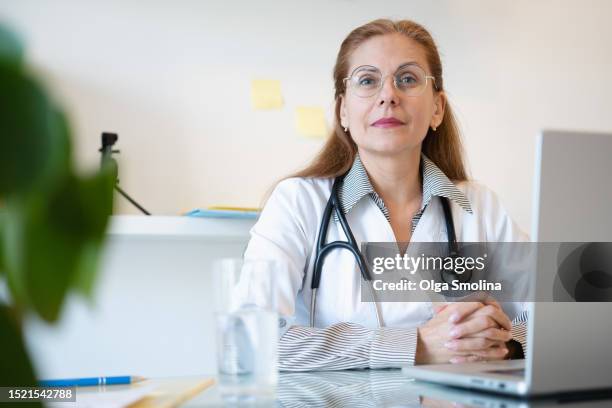 female doctor sitting at desk in doctor's office looking at camera - doctor government stock pictures, royalty-free photos & images