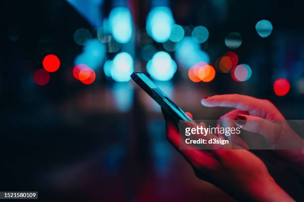 young woman networking with social media on smartphone in city street at night. defocus street lights in background. close up of woman checking social media on smartphone in the city. people engaging in networking with technology. lifestyle and technology - social media advertising stock pictures, royalty-free photos & images