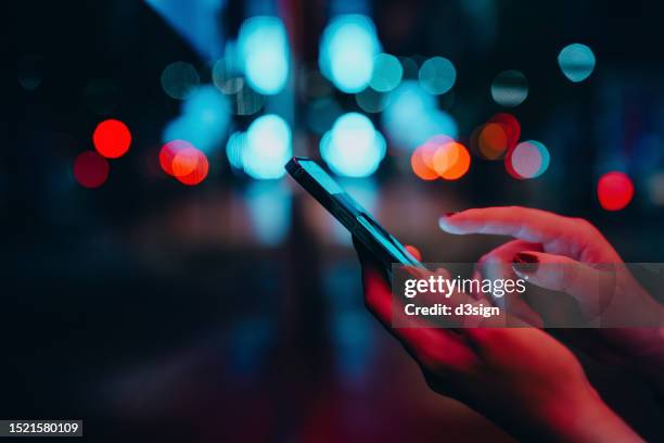 young woman networking with social media on smartphone in city street at night. defocus street lights in background. close up of woman checking social media on smartphone in the city. people engaging in networking with technology. lifestyle and technology - advertisement stock pictures, royalty-free photos & images