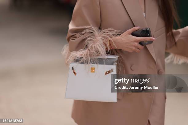 Guest seen outside Elie Saab show wearing gold Cartier love bracelet, white Hermes Kelly bag with gold hardware, Apple iPhone 14 Pro and nude colored...