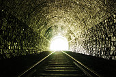 Light at the end of a brick tunnel with train tracks