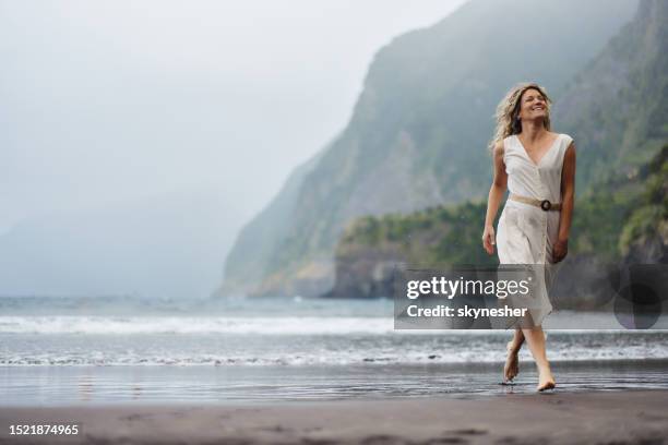 mujer feliz corriendo en la playa durante el día lluvioso. - vestido blanco fotografías e imágenes de stock
