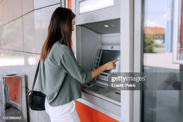 young woman using atm machine - geldautomaat stockfoto's en -beelden