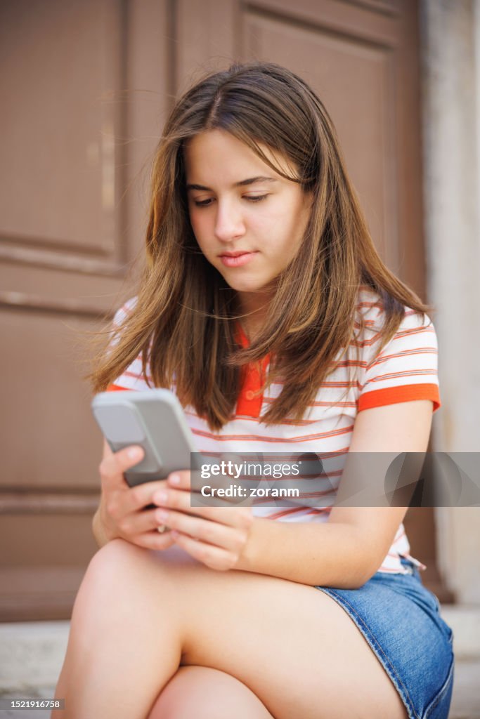 Teenage girl sitting on old house doorway and using smart phone