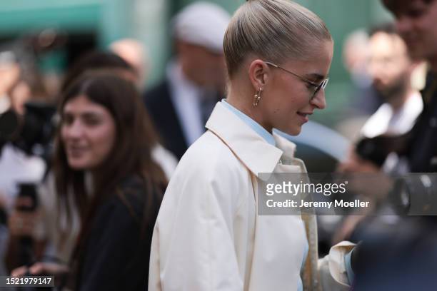 Caroline Daur is seen wearing sunglasses with green lenses, golden earrings from Tiffany & Co. HardWear collection, a creme-white long coat with...