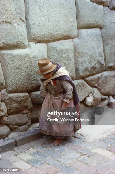 Quechua woman in Colonial-period dress walking past typical Inca Masonry in the famous Inca Street of Hatun Rumiyoc, Cuzco, Peru. Inca. Cuzco.