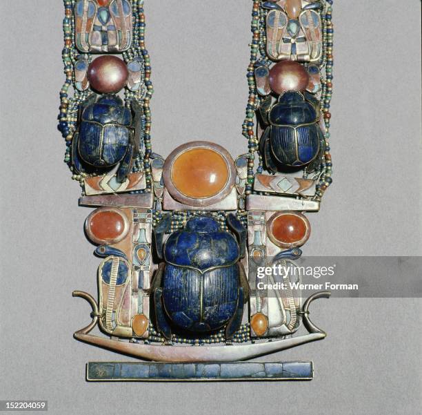 Scarab pectoral from the tomb of Tutankhamun with straps formed from inlaid plaques with uraei , scarabs & solar discs, The pendant is in the form of...