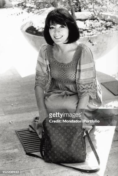 Portrait of the French singer and actress Juliette Greco smiling with a Louis Vuitton handbag. Rome, 1970s