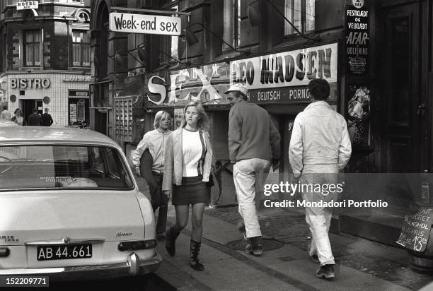 Boy is looking at a girl wearing a mini skirt on a street of Copenhagen. Next to them one of the most spread porn shop of Leo Madsen, who has...