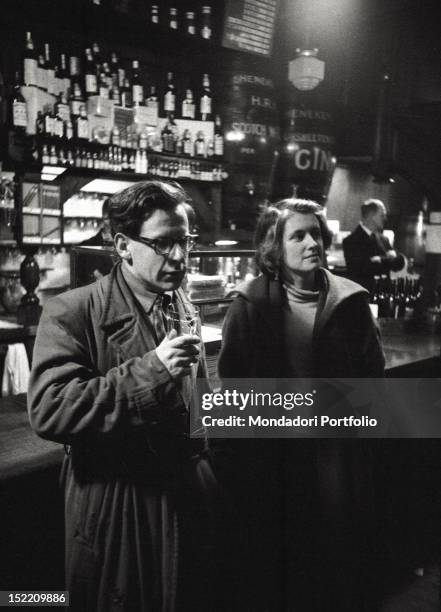 Man with a glass of beer and a woman in front of the bar of a London pub. London , 1957.