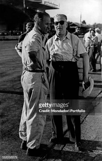 Italian entrepreneur and racing driver Enzo Ferrari having a talk with French racing driver Raymond Sommer on the side of the track. 1940s