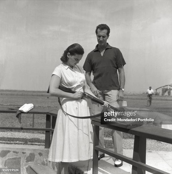 Lucia Bosè, with her husband Luis Miguel Dominguin, is in a shooting range; the actress holds a rifle in her hand. Venice, 1956.