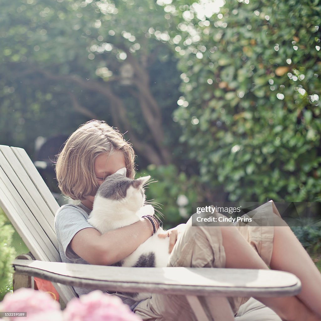 Blond boy in a garden chair cuddling his cat