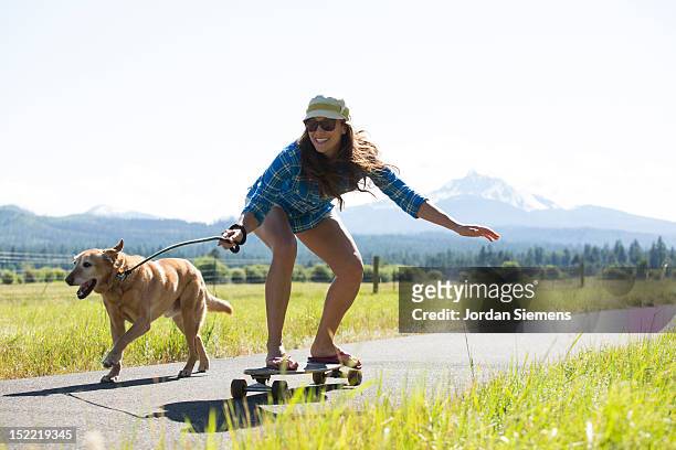 a woman skateboarding with her dog. - dog skateboard stock pictures, royalty-free photos & images