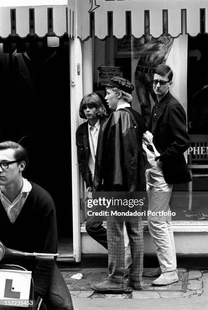 Group of British young mods waiting outside John Stephen's clothes shop. They wear Clarks shoes, tartan trousers, leather jacket and hats in the...