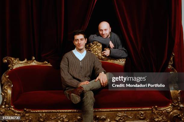 Portrait of Italian fashion designers Domenico Dolce and Stefano Gabbana sitting on a red velvet sofa. 1980s