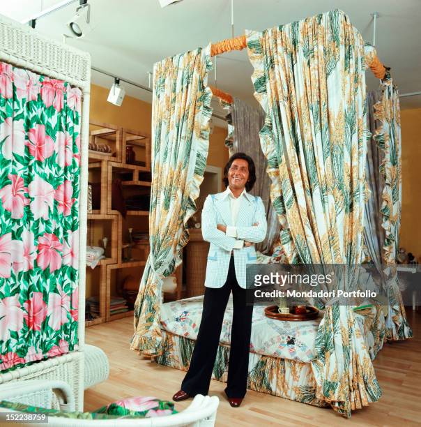 The Italian stylist Valentino standing in his atelier in front of a four-poster bed designed by him in the 'Old America' style. Rome, 1972