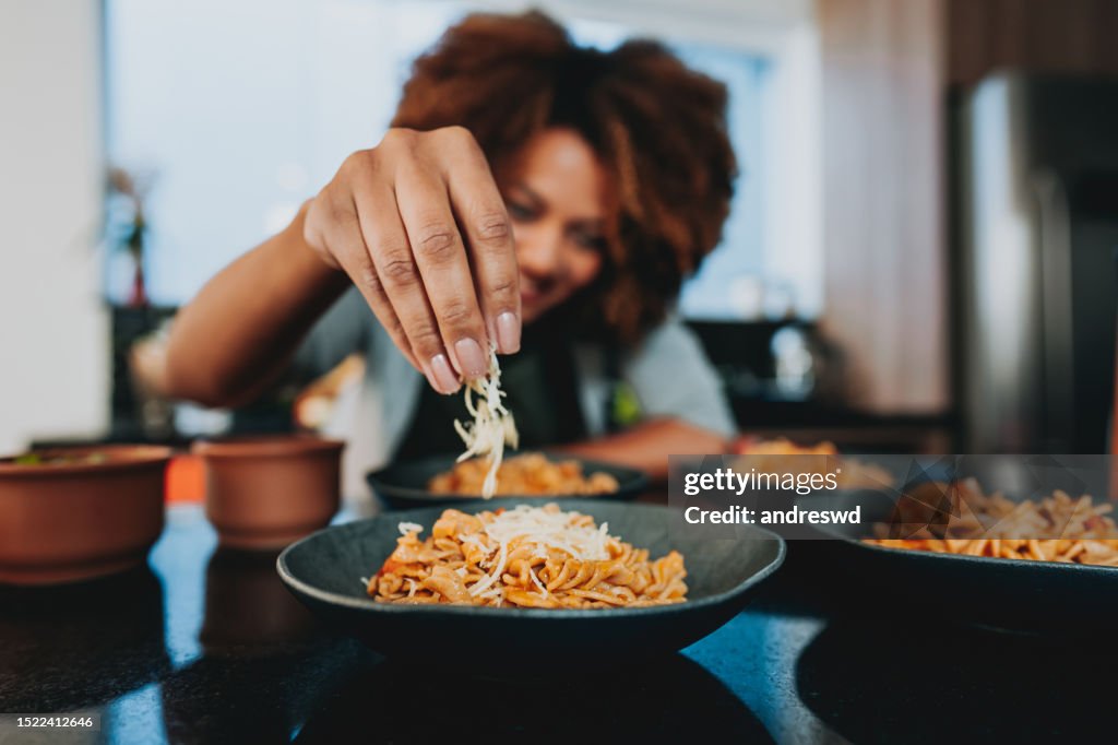 Woman putting grated cheese on macaroni
