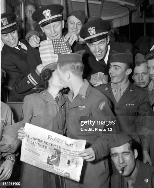 Holding a copy of a special edition of France Soir, a US soldier kisses a W, A, C corporal, in Paris, learning the news August 10 that the Japanese...