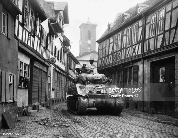 German civilians watch from their windows as a tank of the 4th Armored Division, 3rd US, Army, drives through a street in Hanau .